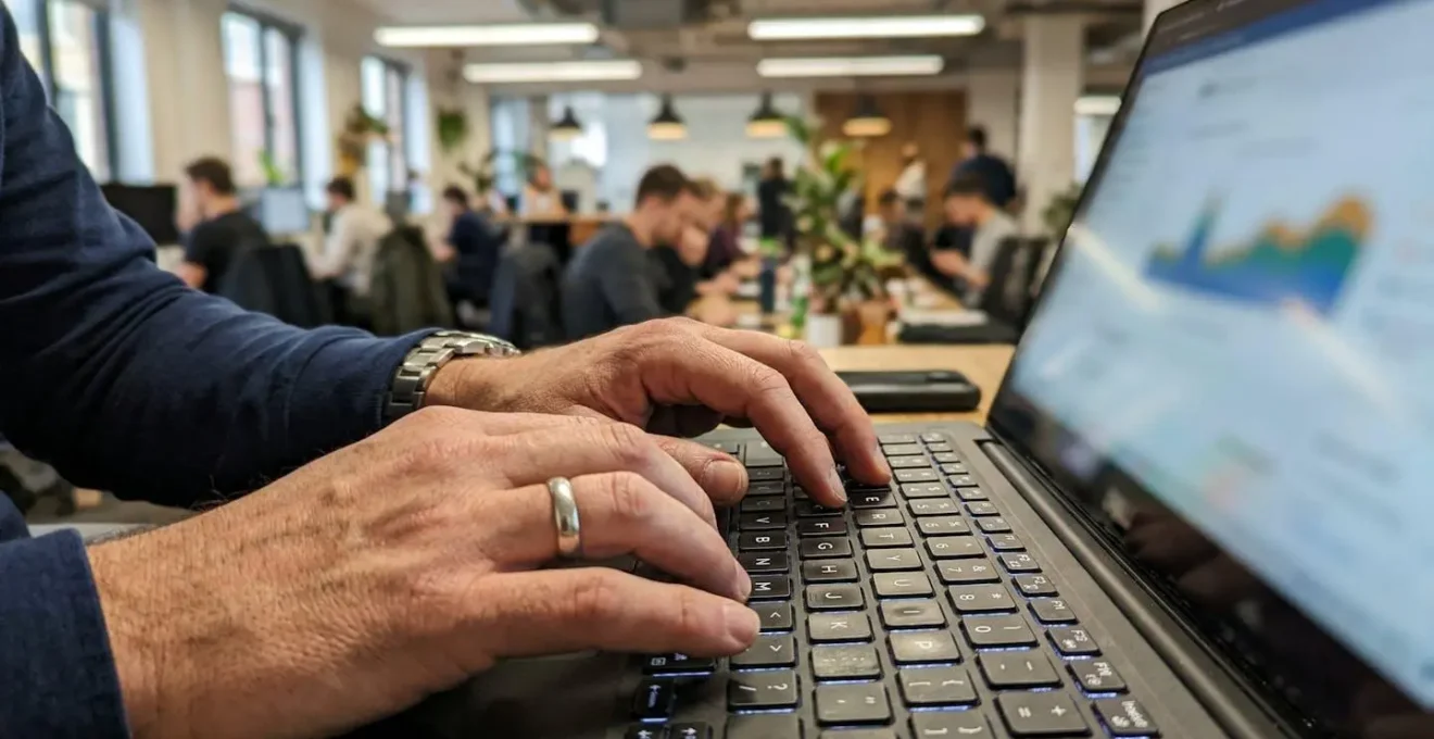 Gros plan sur des mains tapant sur un clavier de laptop dans un environnement de bureau moderne, écran affichant un graphique totalement flouté